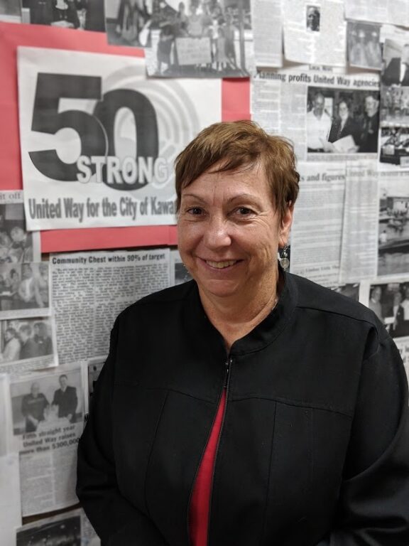 An image of a woman in a black sweater standing in front of a board full of black and white images