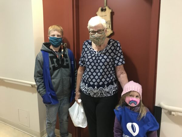 Two children posing with a woman as they deliver her a card